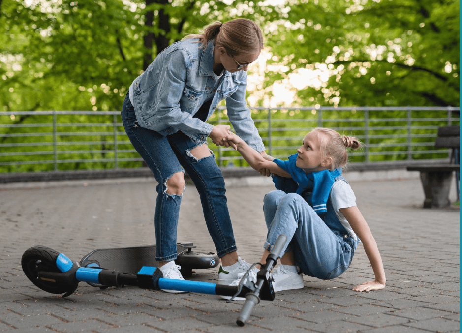 moteris padeda mažai mergaitei, kuri nuo paspirtuko nukrito